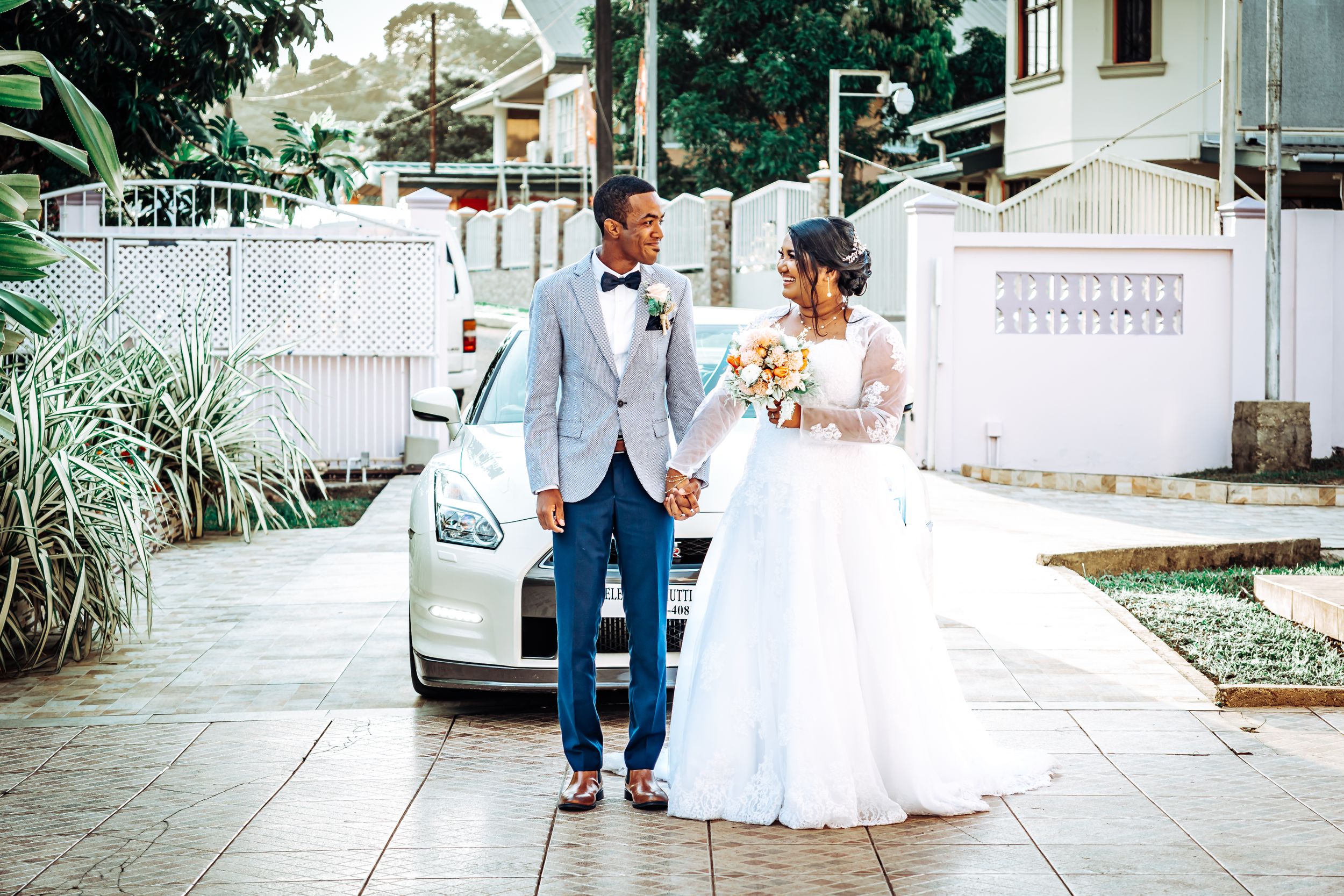 Wedding couple walking together on sidewalk with tropical landscaping in background.