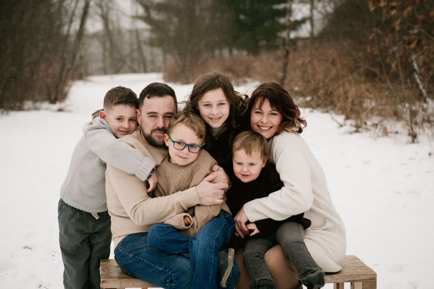 A group sits together outdoors on a snowy winter day wearing coordinated neutral-colored sweaters and casual attire.