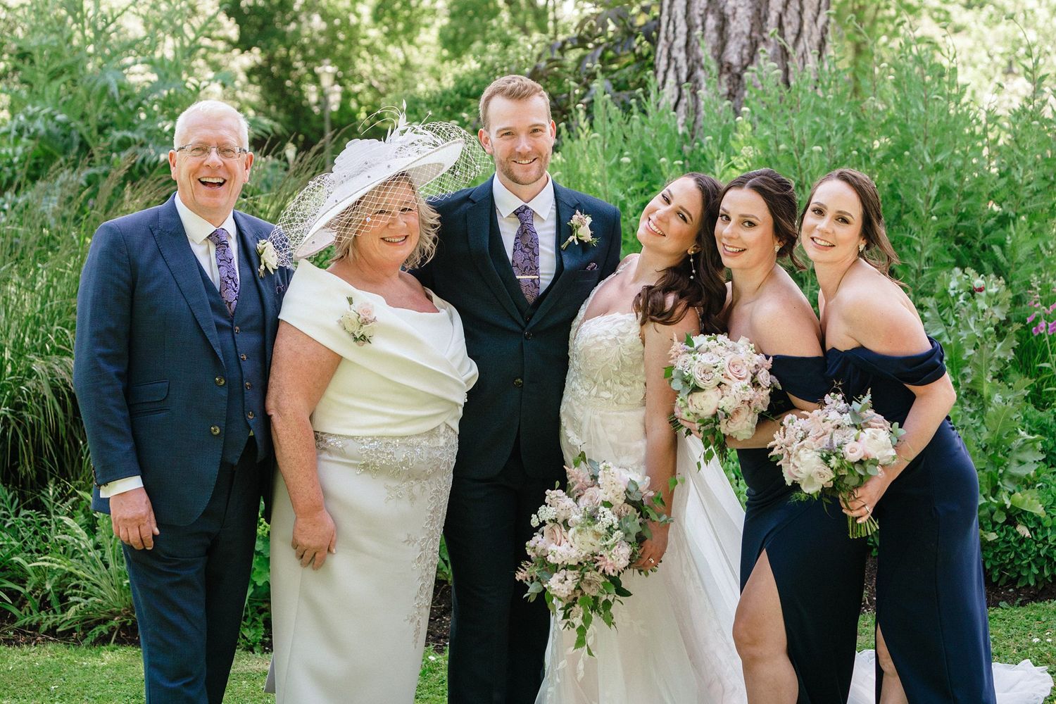 Wedding party poses in Halifax, NS outdoors in formal attire with blue and ivory dresses holding white floral bouquets