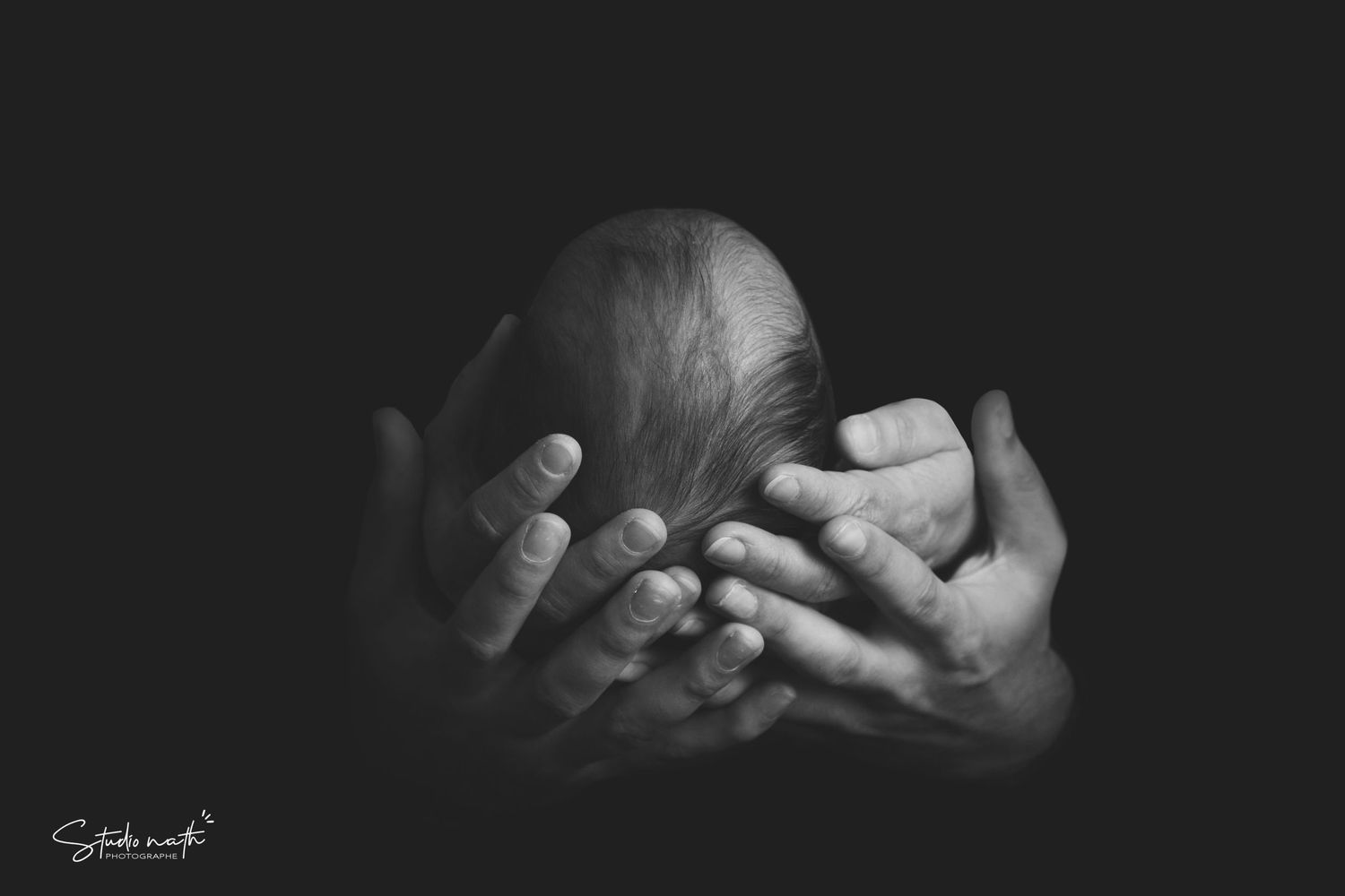 A tender black and white photograph captures the gentle support of hands cradling a baby's head.