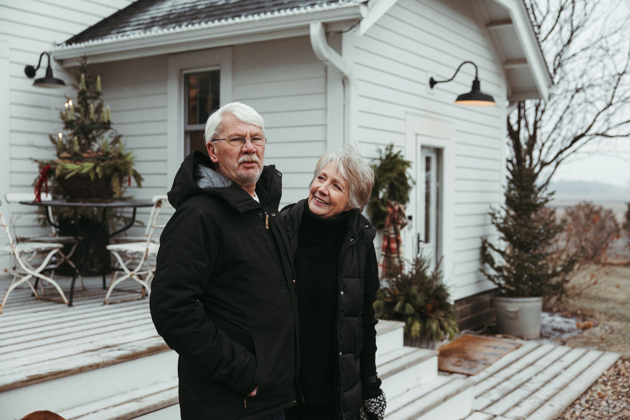 Elderly couple shares a joyful moment together on the front porch of a white house during winter.