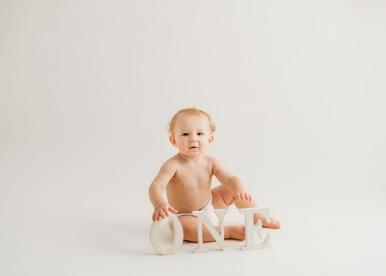 Baby in white diaper sitting beside pastel-colored blocks on clean white background.