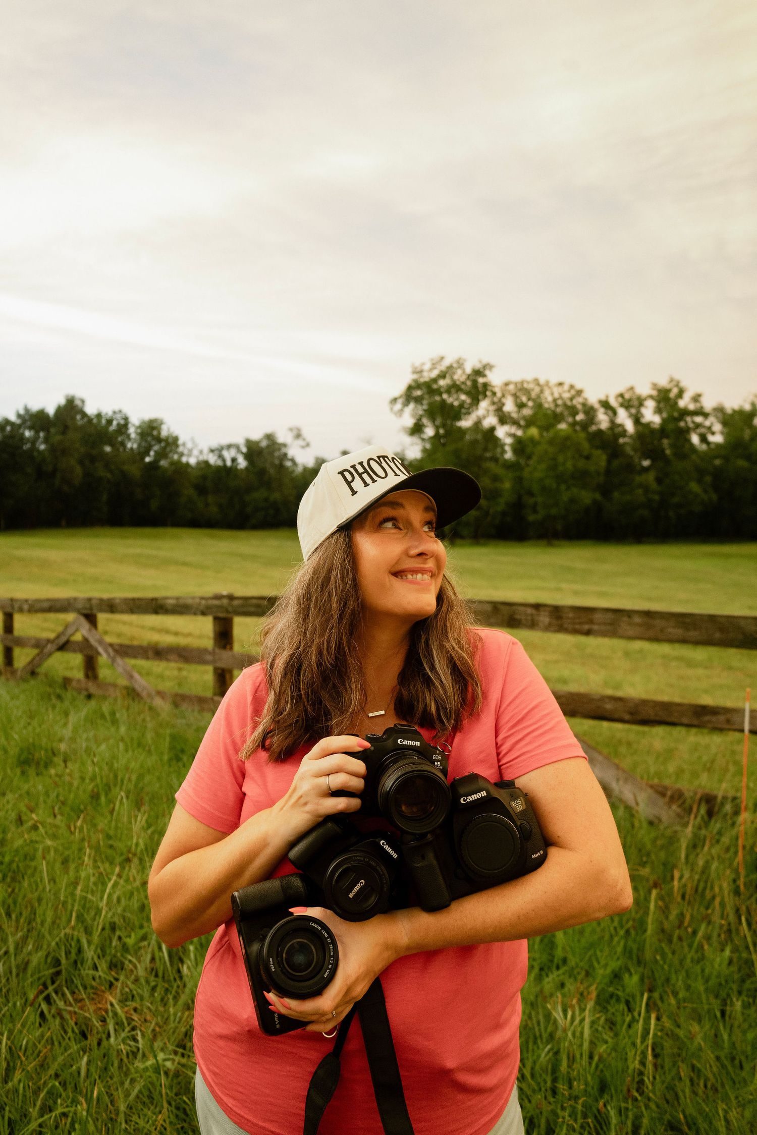 Portrait of Marion photographer Nichole holding various cameras in front of a rustic fence on a summer evening in Cedar Rapids.