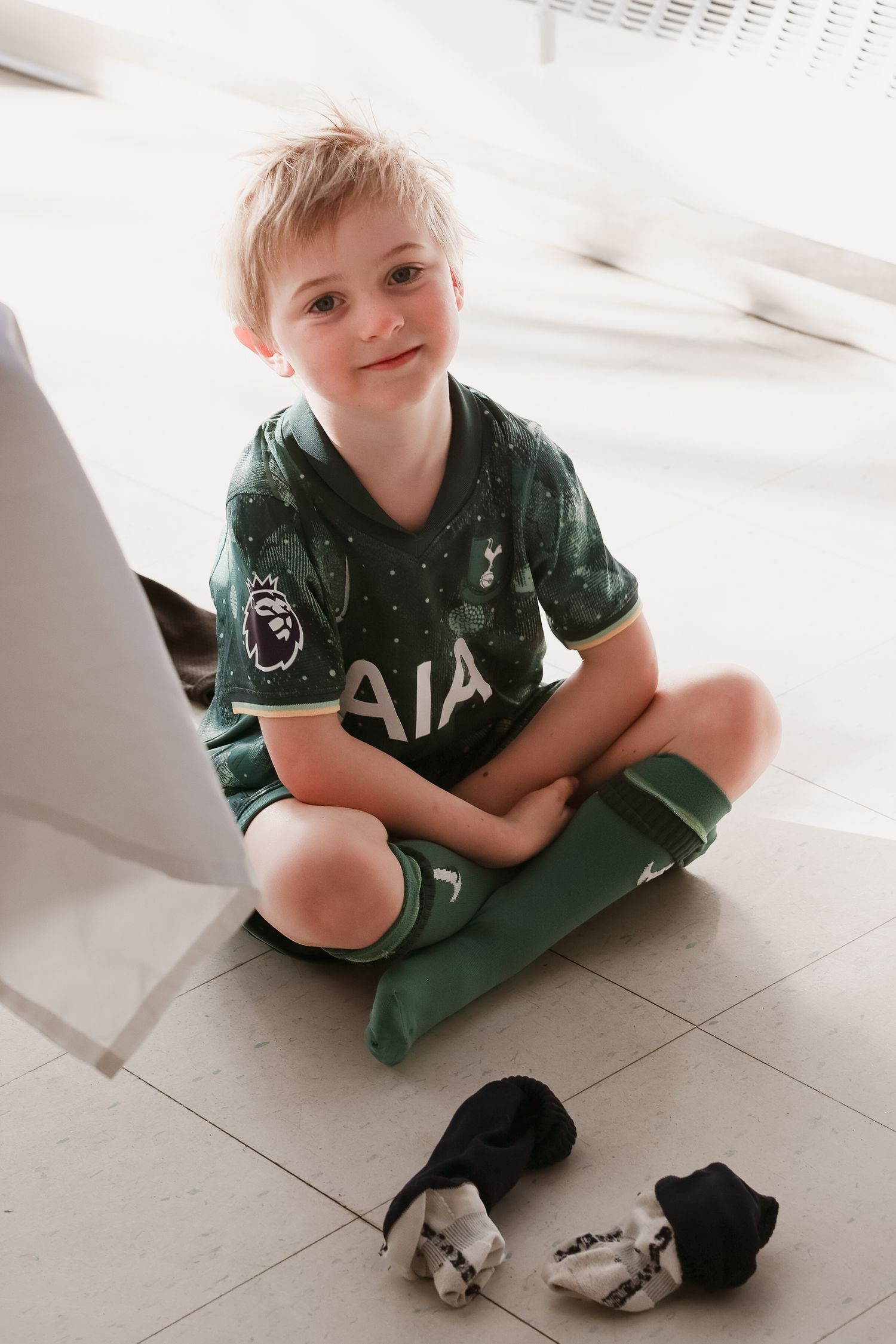 Child sitting cross-legged on floor wearing green Tottenham Hotspur jersey. Event and Birthday Photography by Smilein.