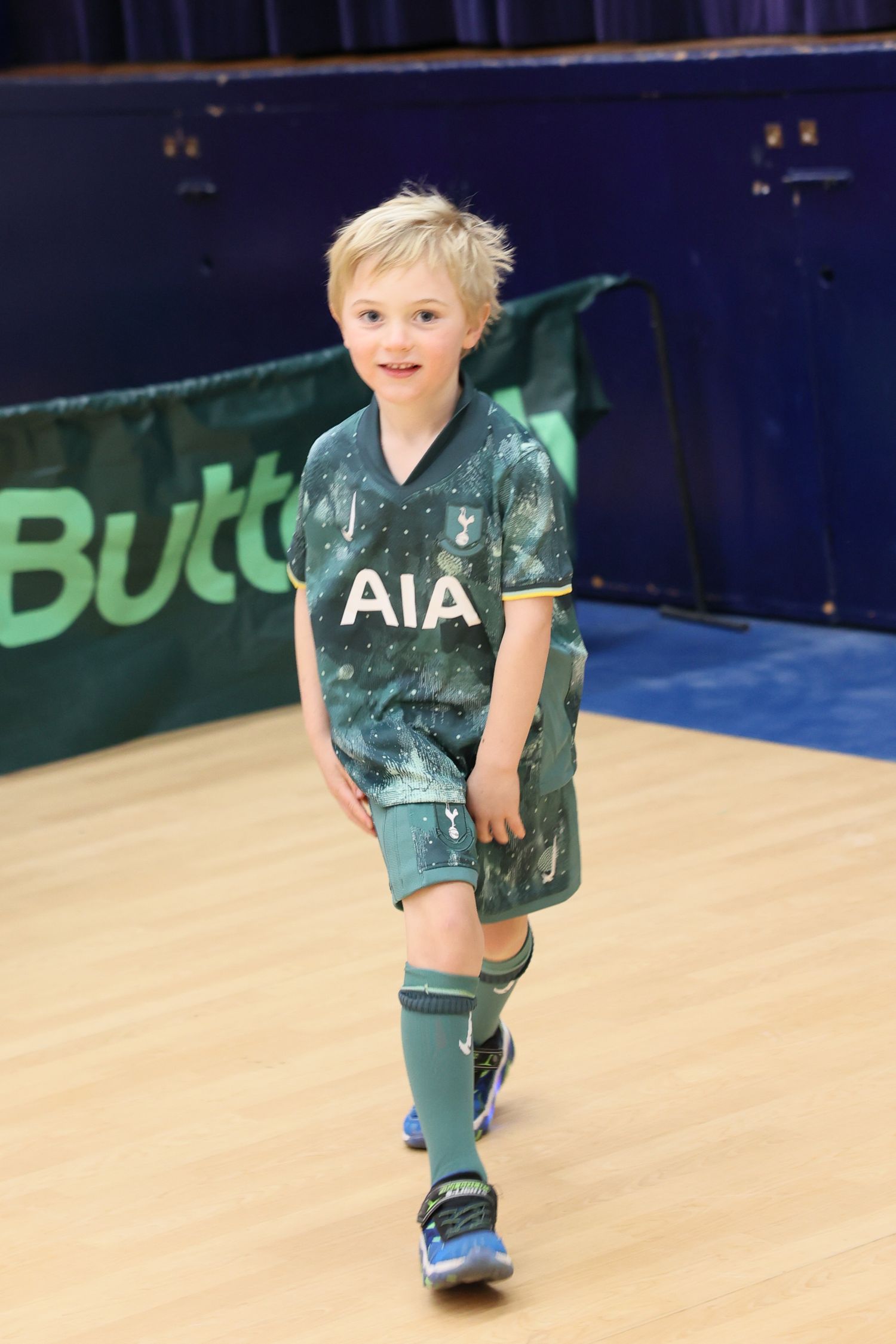Young athlete in a teal AIA soccer uniform poses on an indoor court. Event and Birthday Photography by Smilein.