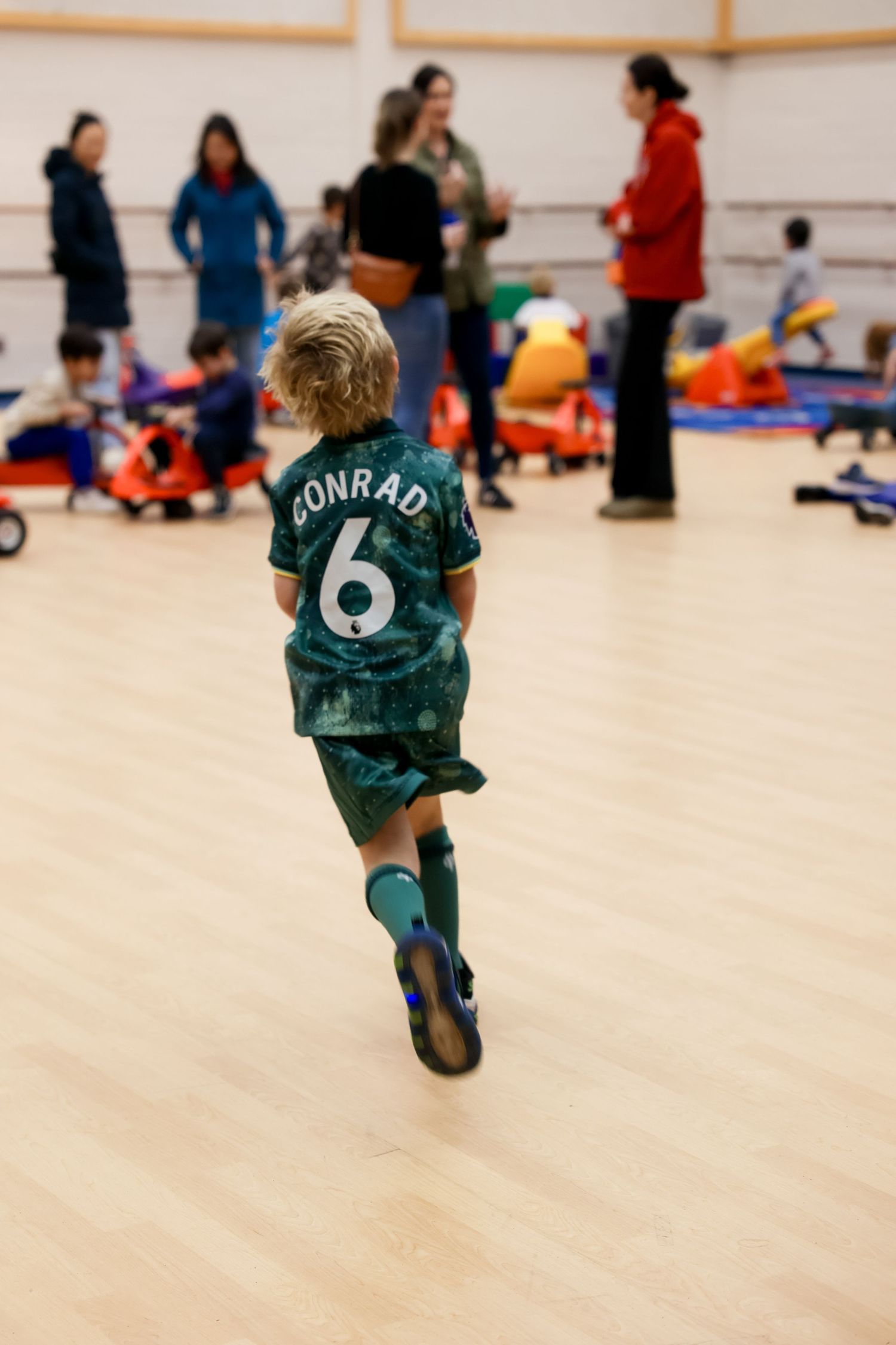 Young player wearing soccer jersey runs across indoor gym floor during youth sports activity.Event and Birthday Photography by Smilein.