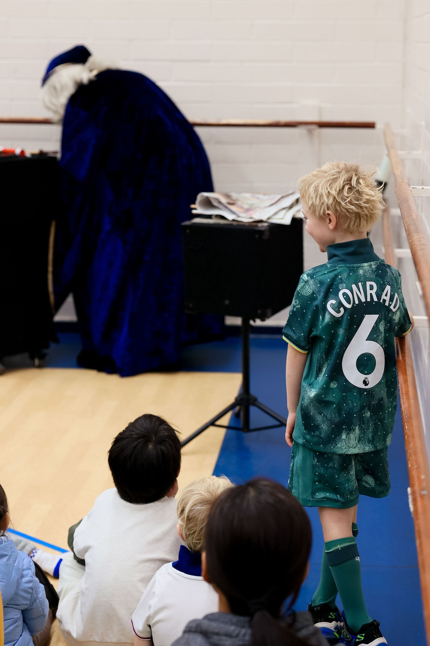 Young soccer player wearing number 6 jersey stands watching a game in an indoor sports facility.Event and Birthday Photography by Smilein.