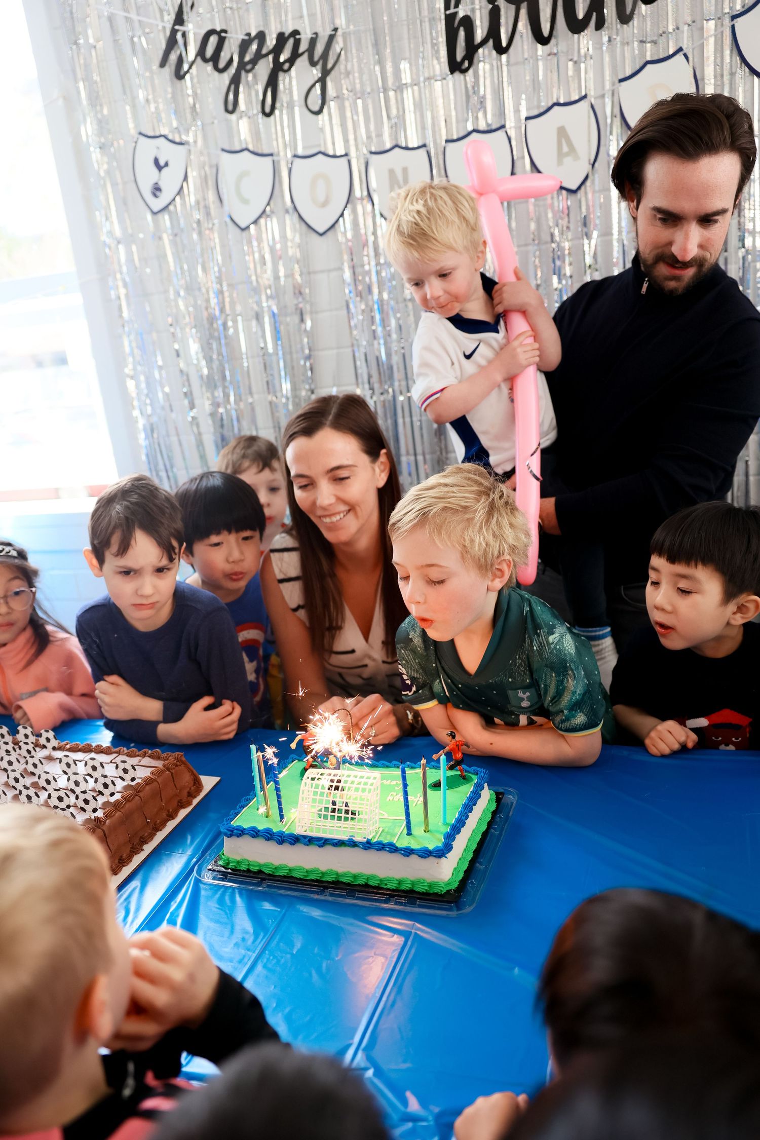 Birthday party with a decorated cake glowing with candles while children gather around at a party.Event and Birthday Photography by Smilein