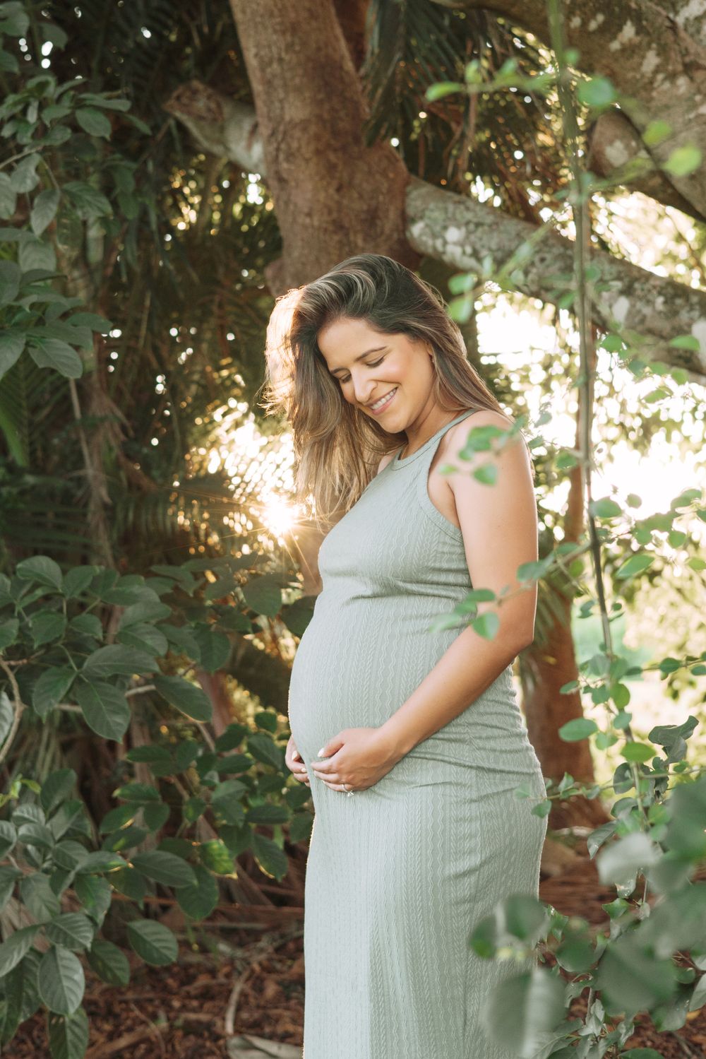 Serene maternity portraits showing pregnant woman in gray dress posing among lush garden foliage.