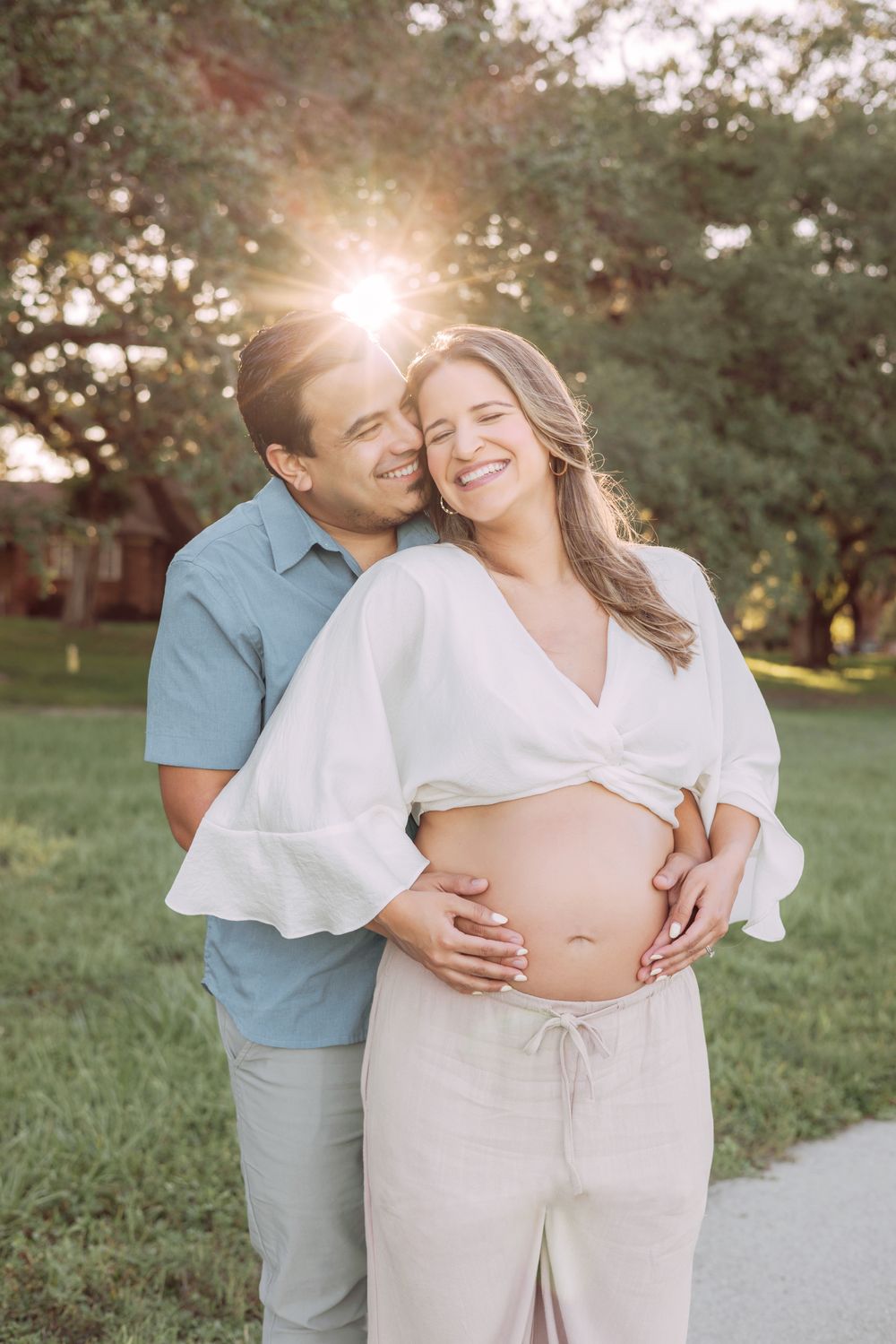 A couple shares an intimate moment outdoors at sunset during a maternity photoshoot in a park.