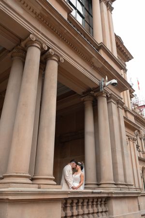 Bride and groom sharing a romantic moment between tall classical columns of a heritage building.