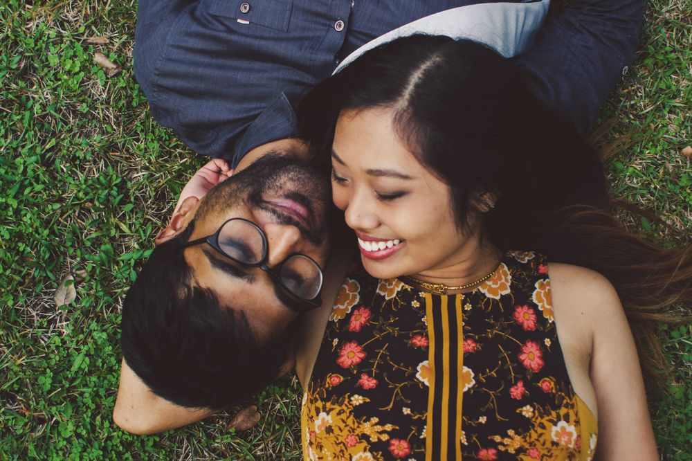 Close-up of couple lying on grass smiling while wearing colorful summer outfits.