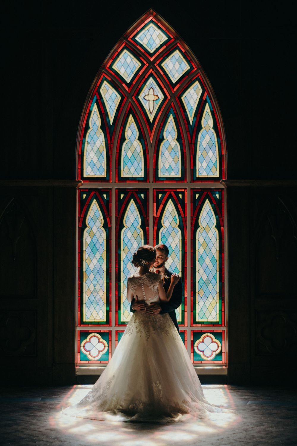 A romantic wedding scene framed by a Gothic stained glass church window creates dramatic lighting.