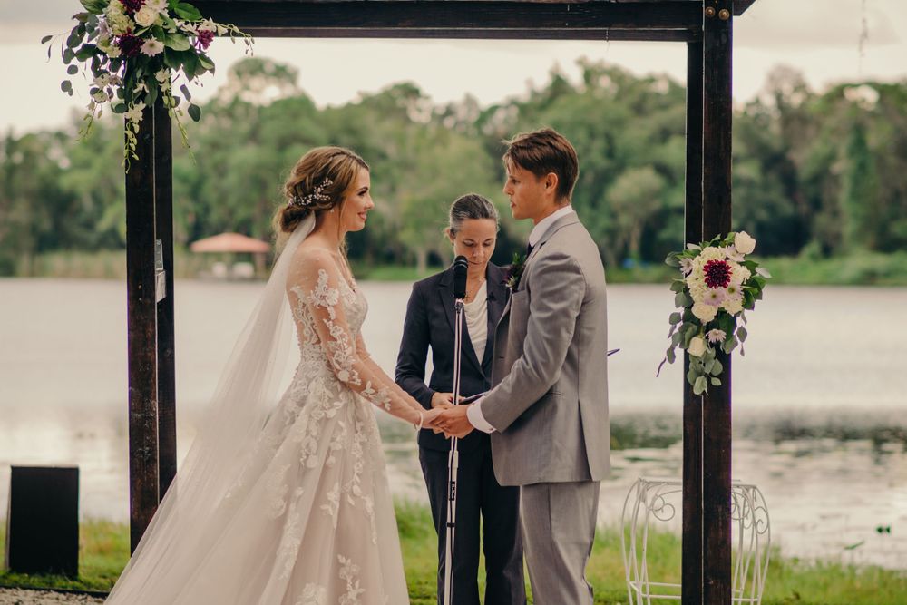 Outdoor lakeside wedding ceremony under black pergola with floral arrangements.