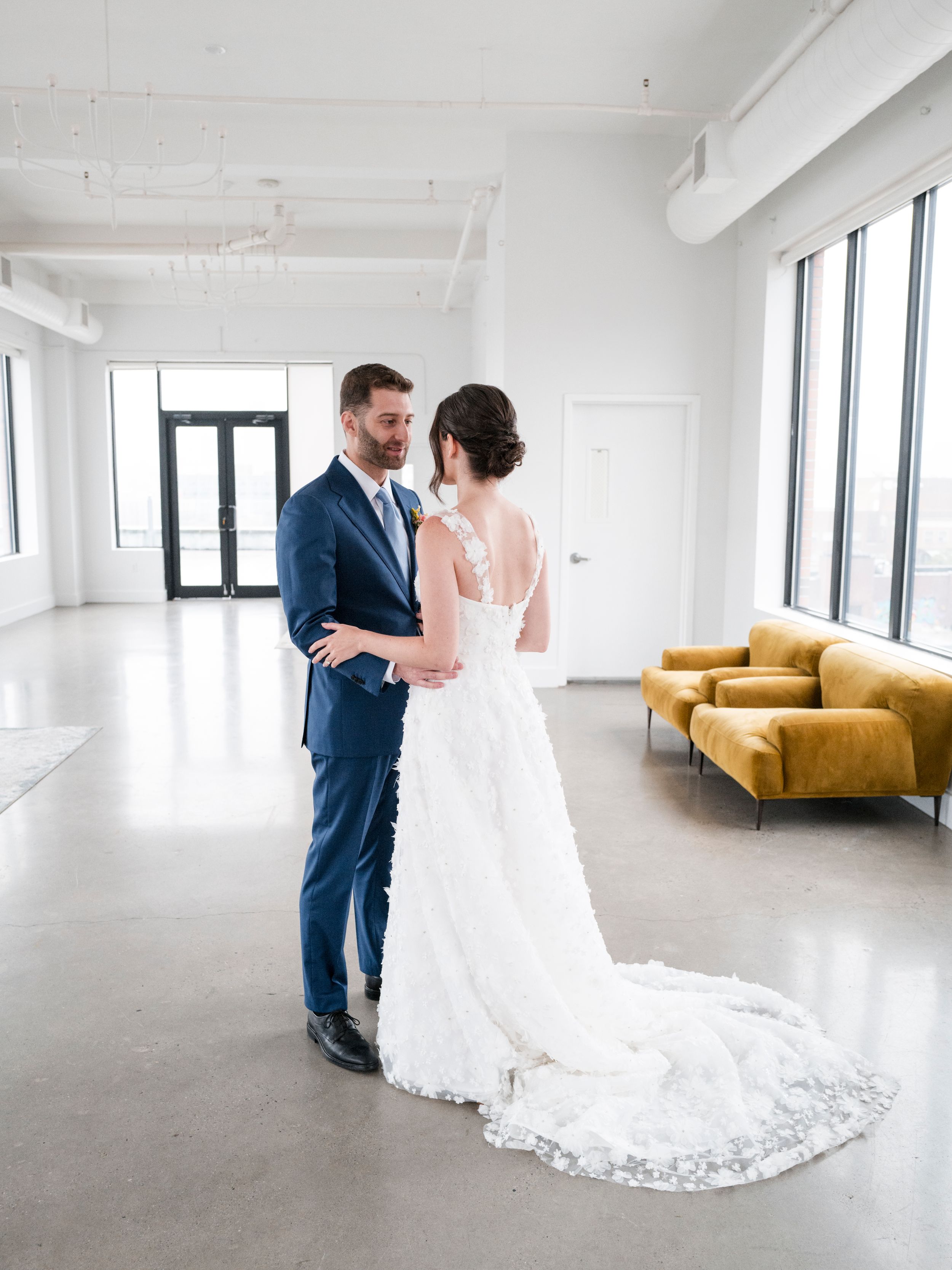 A couple shares their first look in a bright white modern venue with a mustard yellow couch.