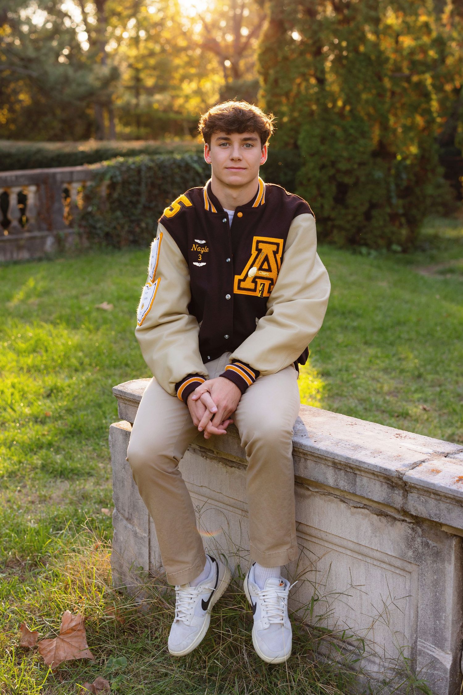 Varsity letterman jacket with cream sleeves and black body worn while sitting on stone wall at sunset.