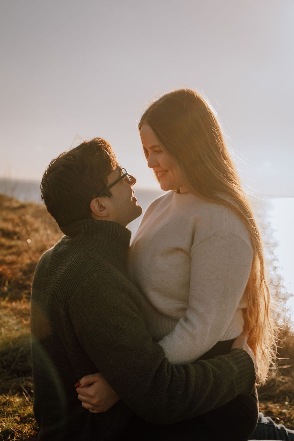 Romantic couple embraces outdoors during golden hour on hillside with sunlit backdrop.