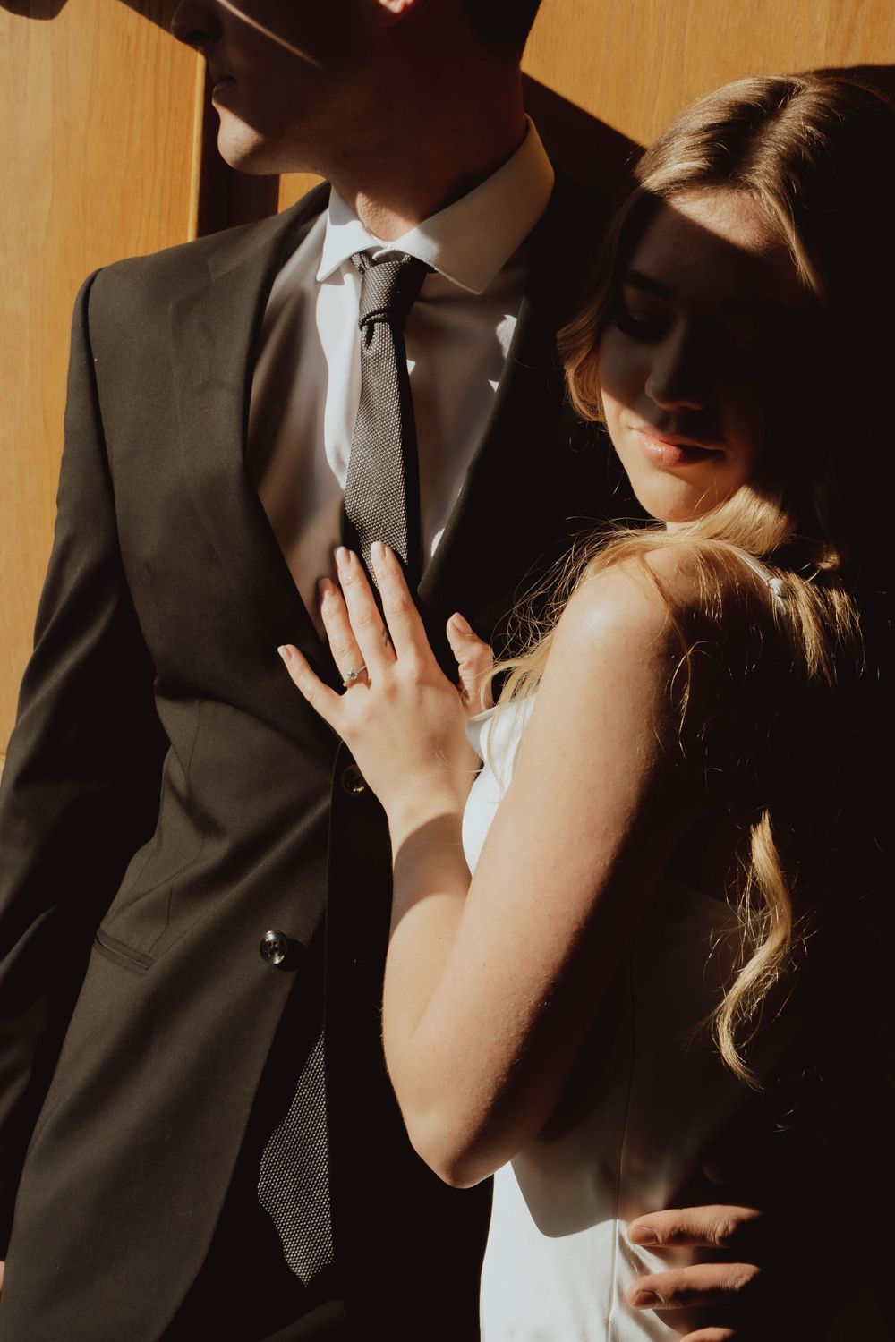A couple in formal attire stands together in dramatic golden sunlight during a romantic photoshoot.