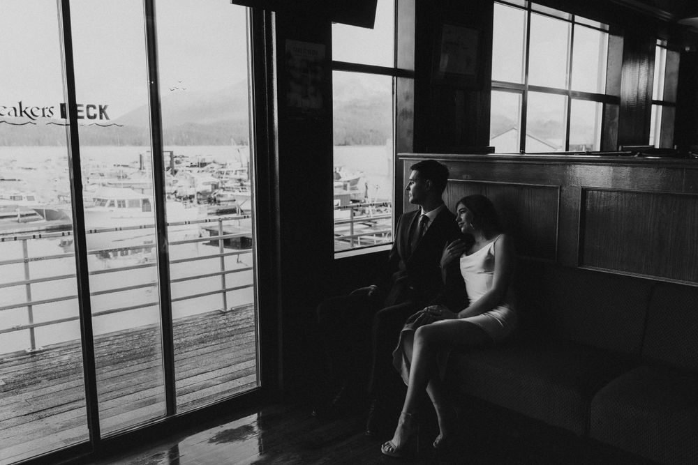A silhouetted figure sits alone by a window in a dark train car, gazing at the passing landscape through glass panes.