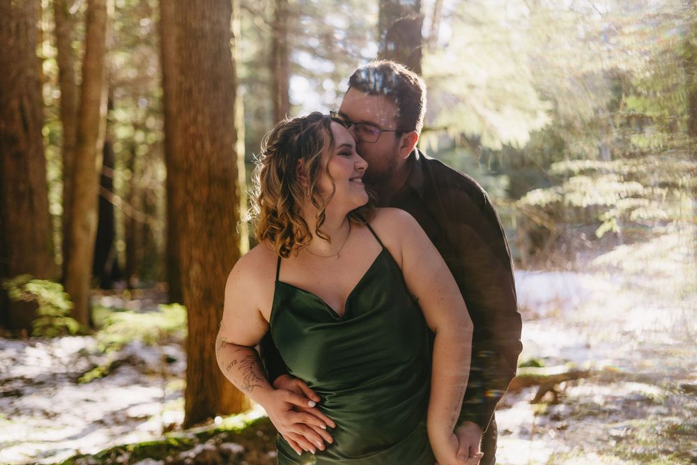 Romantic winter forest scene showing a couple embracing among snow-dusted trees in dreamy natural lighting.