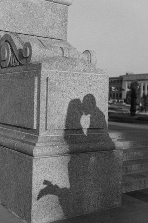 Black and white photo of two silhouettes kissing, their shadow cast on a granite monument base.