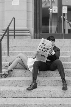 Black and white photo of a couple sitting on steps holding a newspaper reading The Canaways 6.9.28.