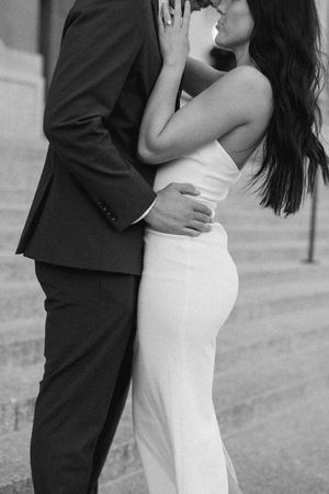 Black and white photo of couple embracing in formal wear, woman in white gown, romantic engagement portrait.