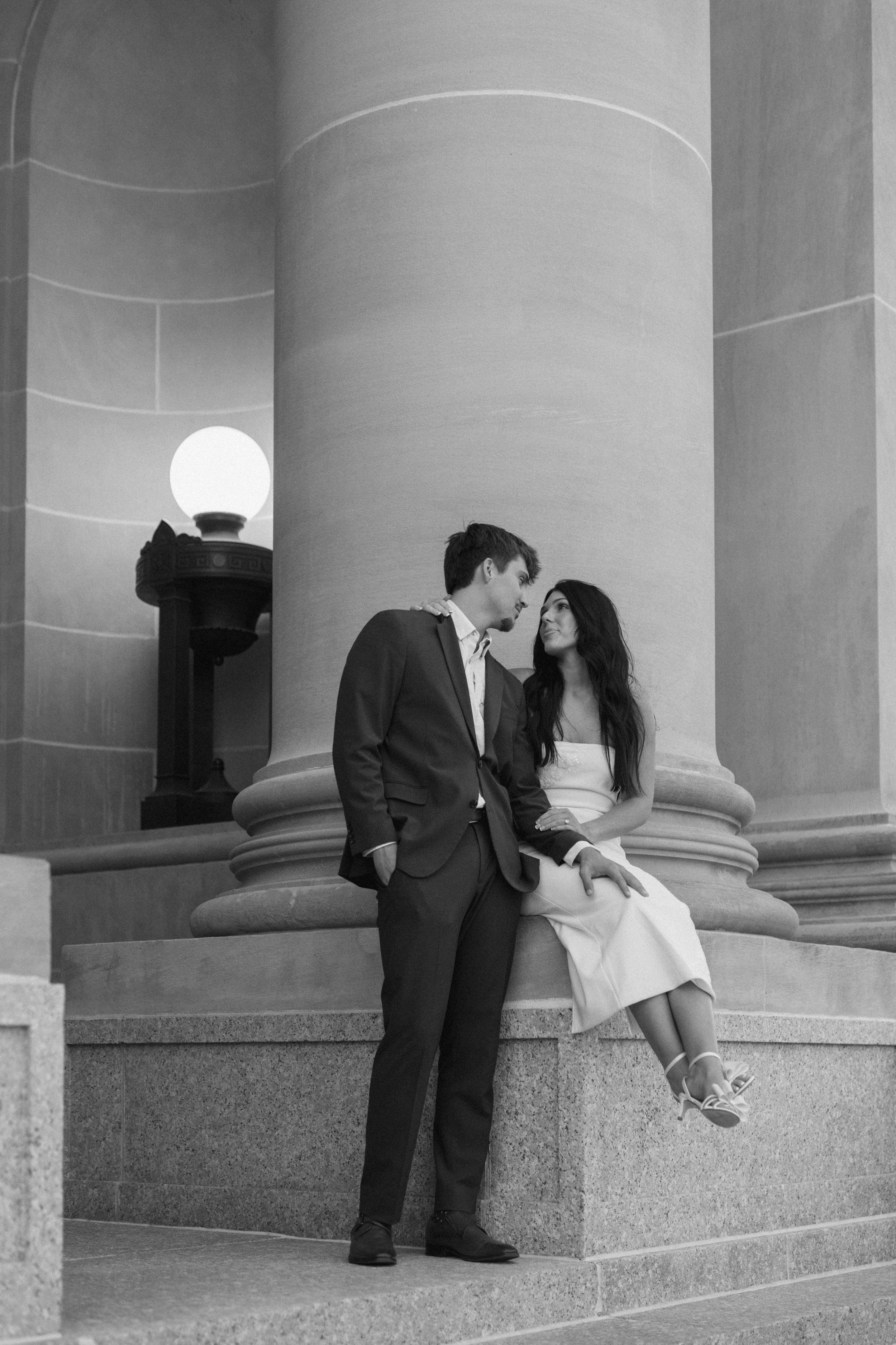 Black and white photo of couple sharing an intimate moment between grand stone columns.