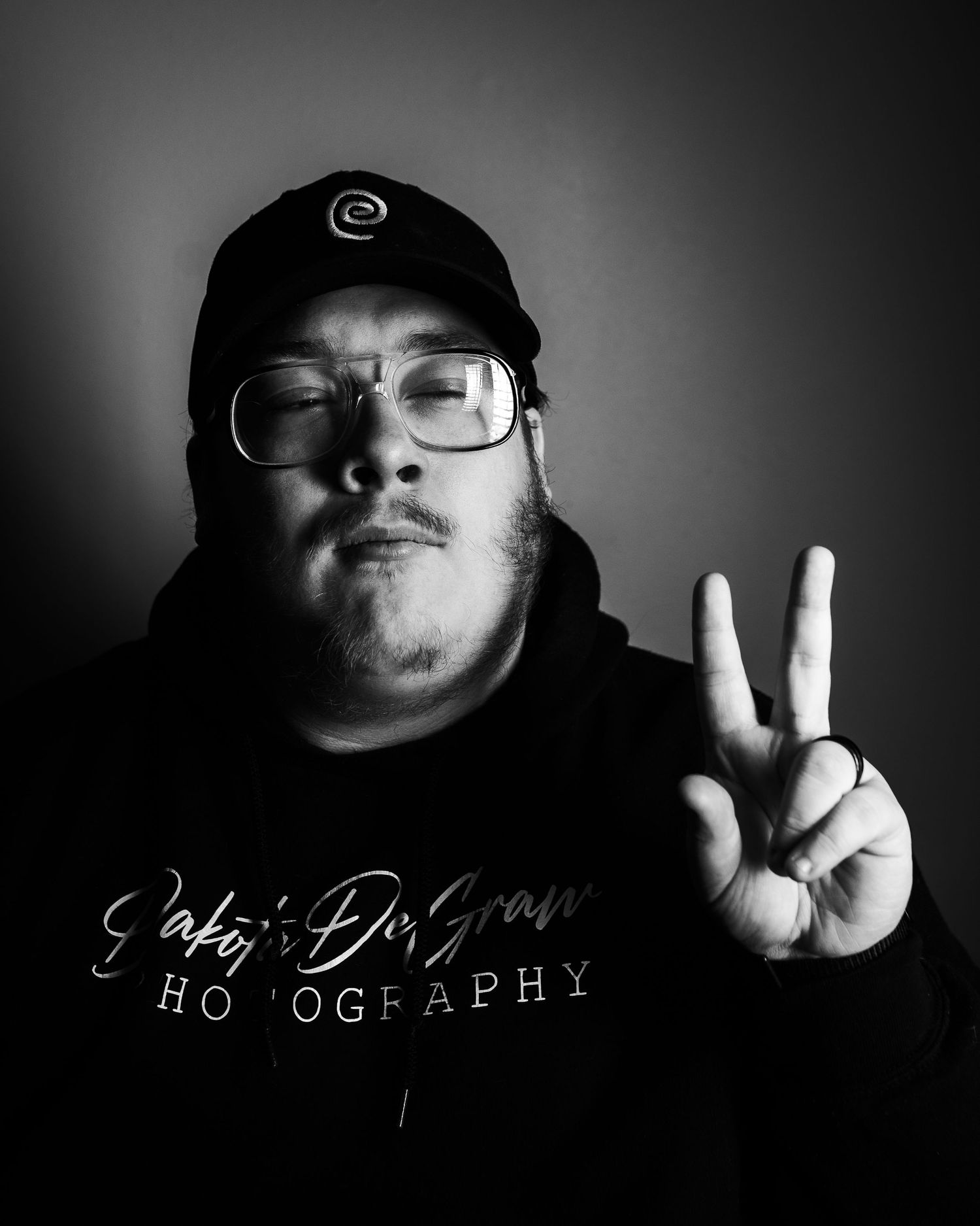 Black and white self-portrait of the owner, Dakota DeGraw, doing a peace sign while wearing his business merch