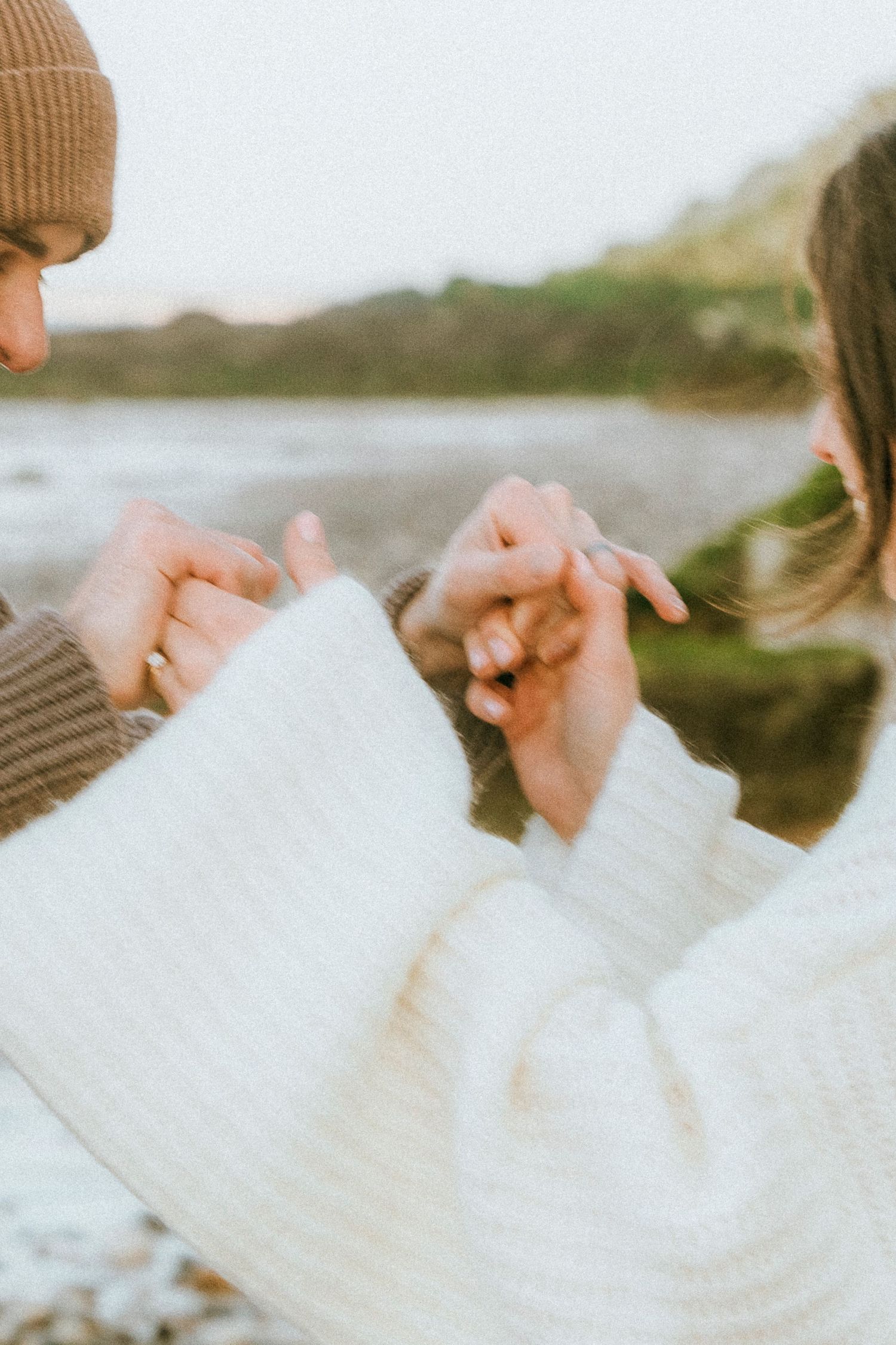 Close up of two people holding hands together outdoors in cozy winter clothing with a blurred background.