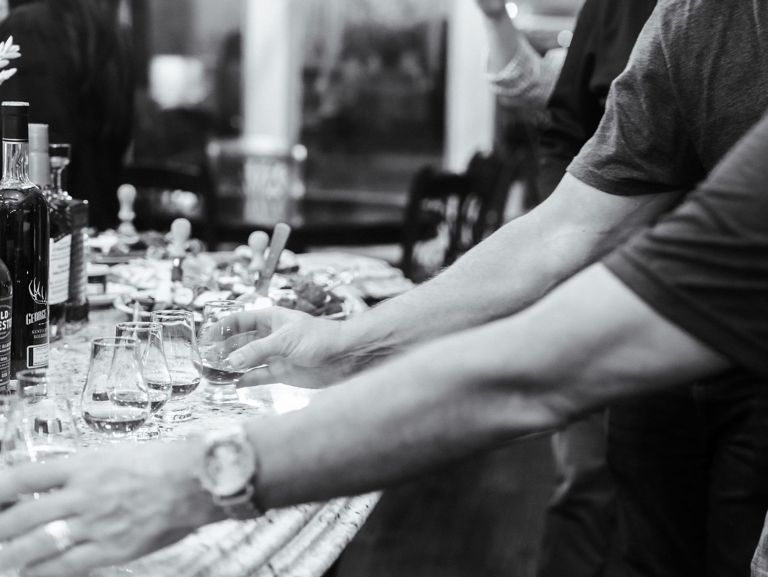 A bartender's arm reaches across a bar counter to arrange wine glasses and place settings in black and white.