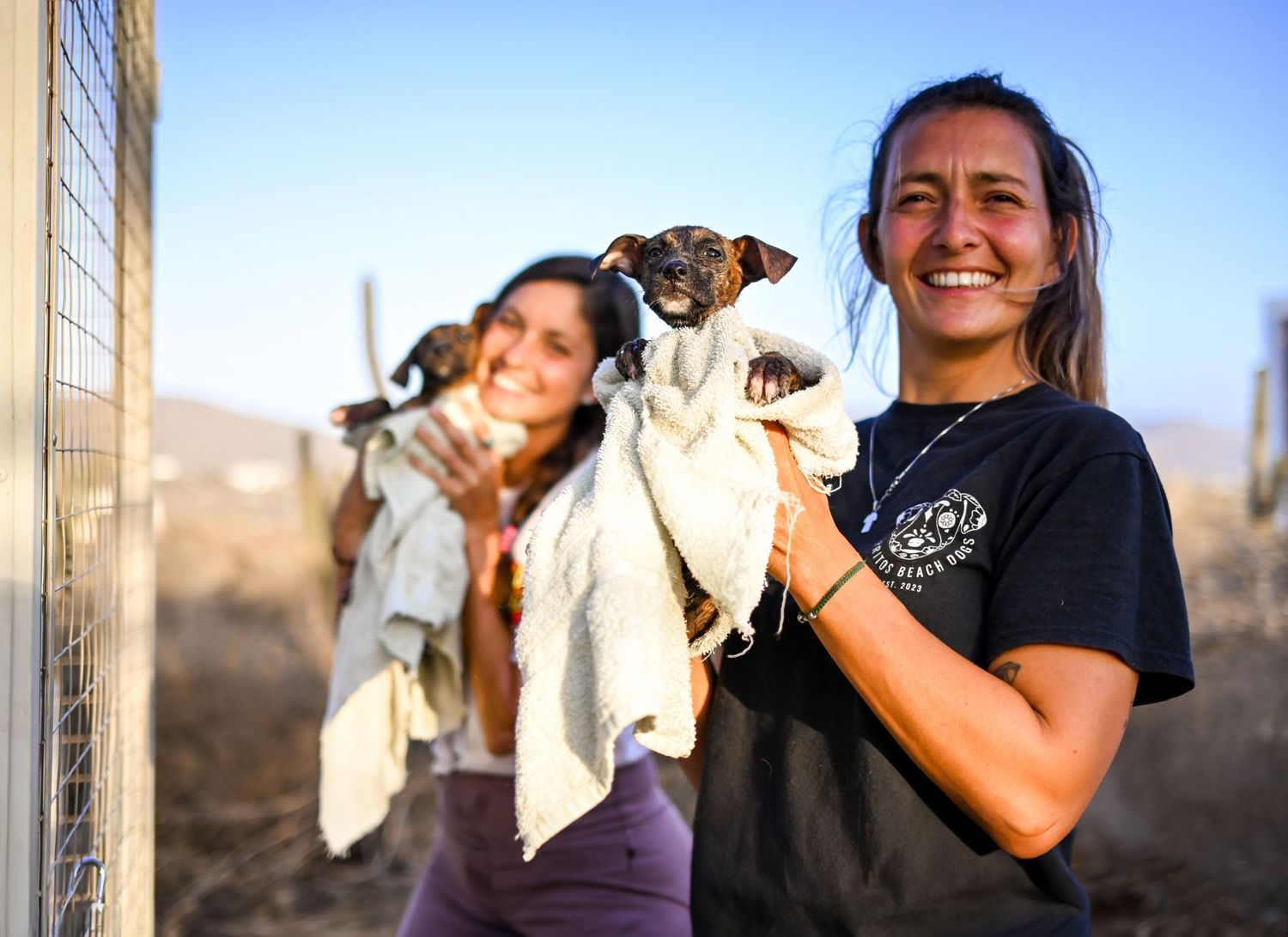 two women hold up rescue puppies wrapped in towels outside