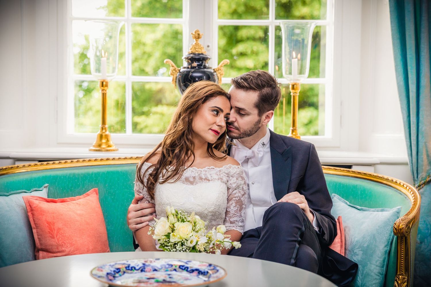 A romantic wedding portrait on an elegant vintage sofa with soft window lighting.