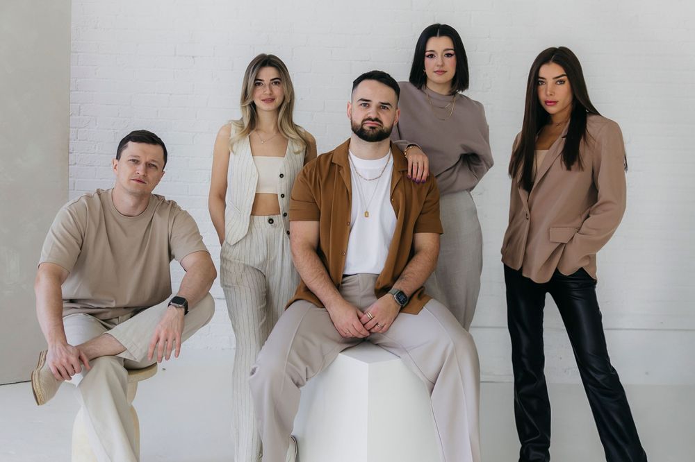 Group photo of models wearing coordinated neutral-toned outfits against white backdrop.