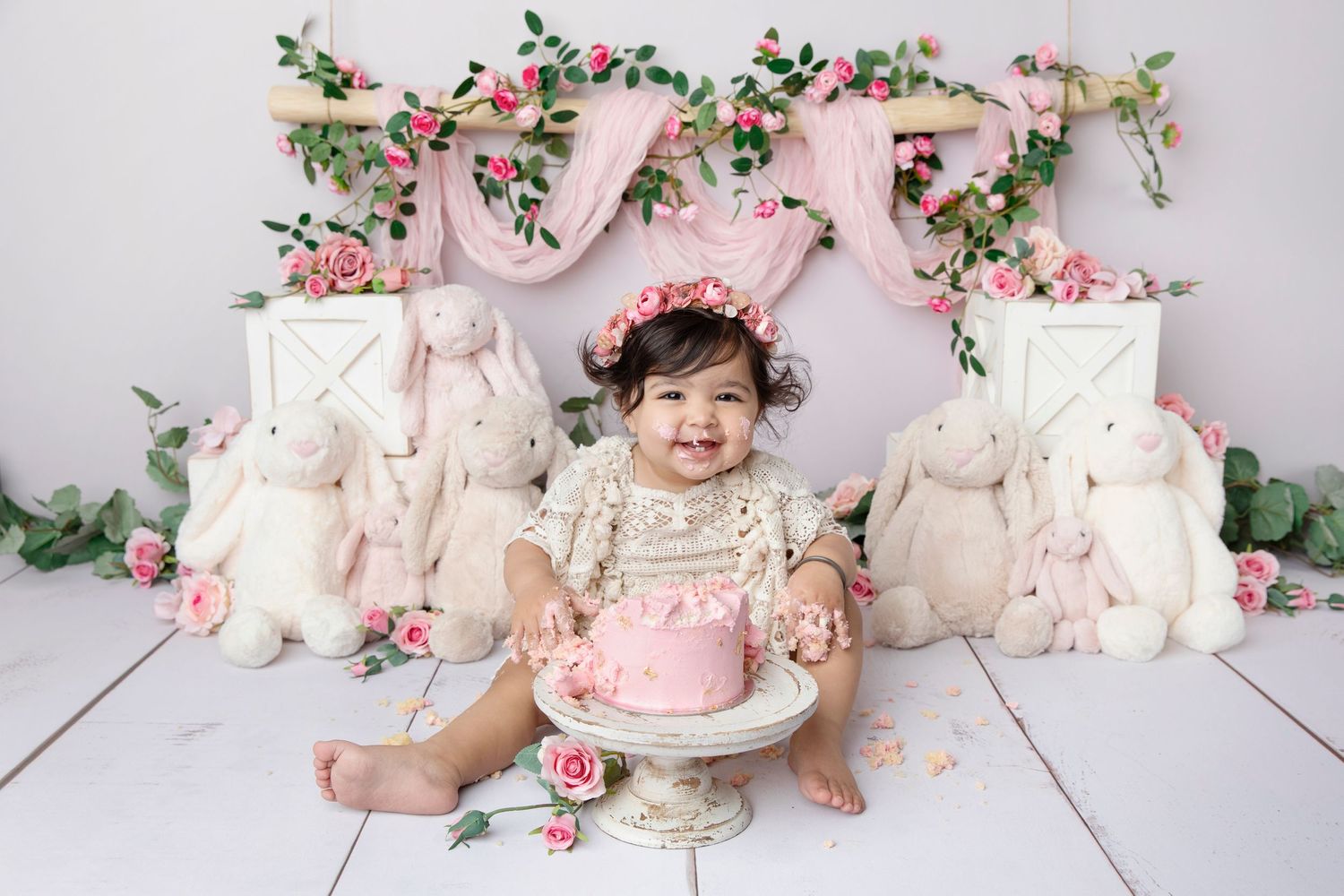 Easter themed setup with baby surrounded by plush bunnies and floral decorations in pink setting.