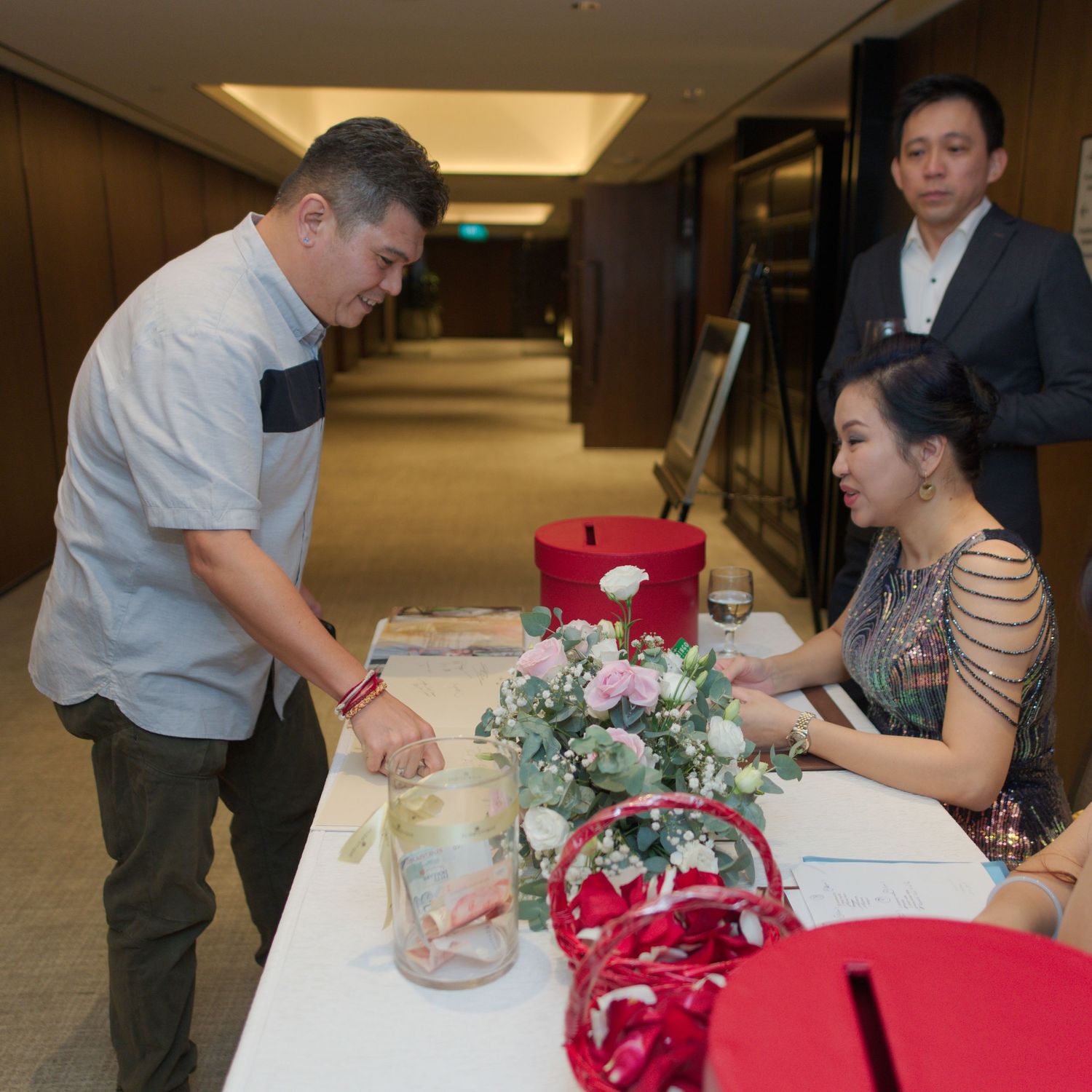 People interacting at a reception table with red decorations and floral arrangements.