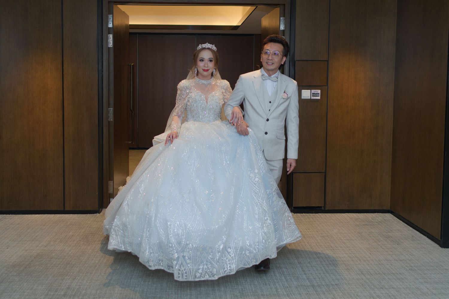 Wedding couple in formal attire standing in hotel hallway.