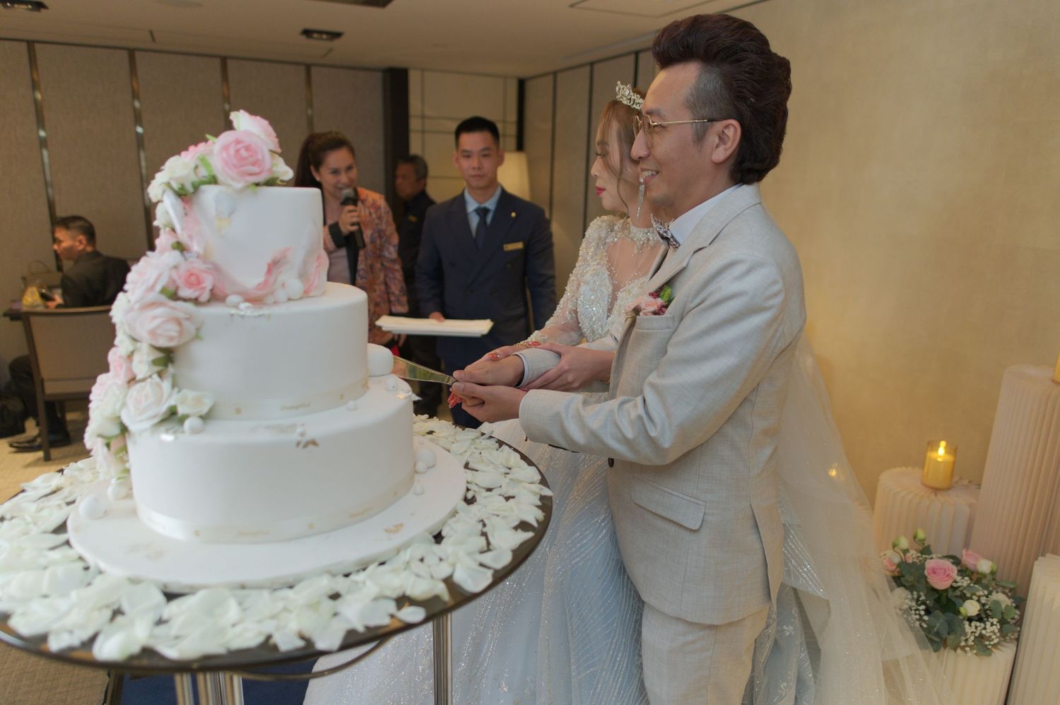 Newlyweds cutting their elegant multi-tiered white wedding cake decorated with pink flowers.