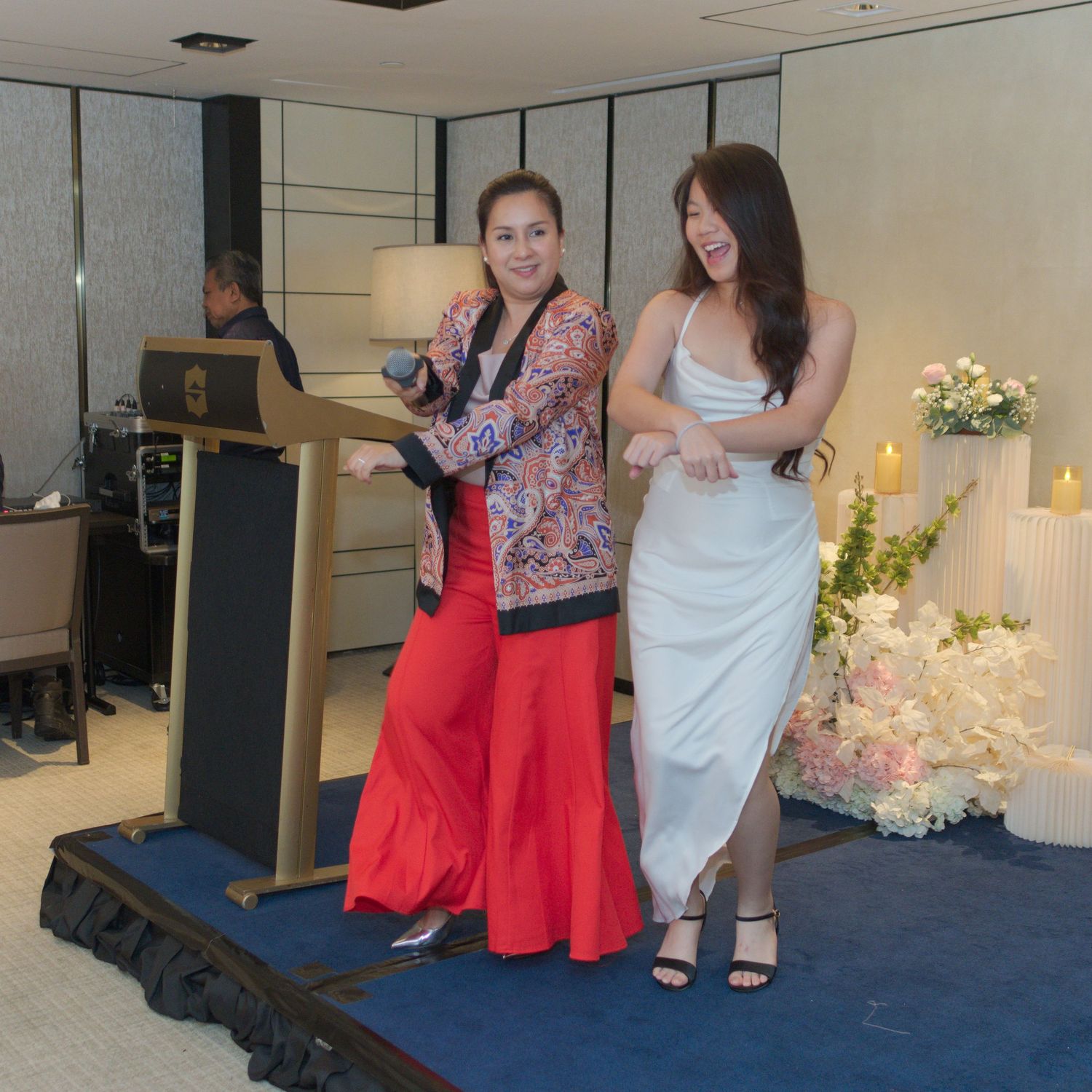 Two speakers presenting at a wedding reception podium with floral decorations.