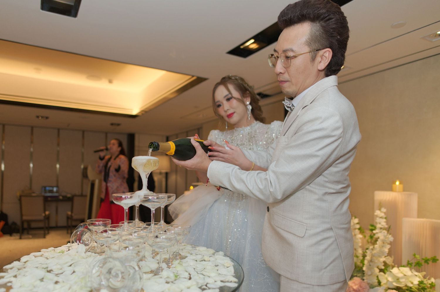 Couple performing a champagne toast at their wedding reception next to a decorated cake table.