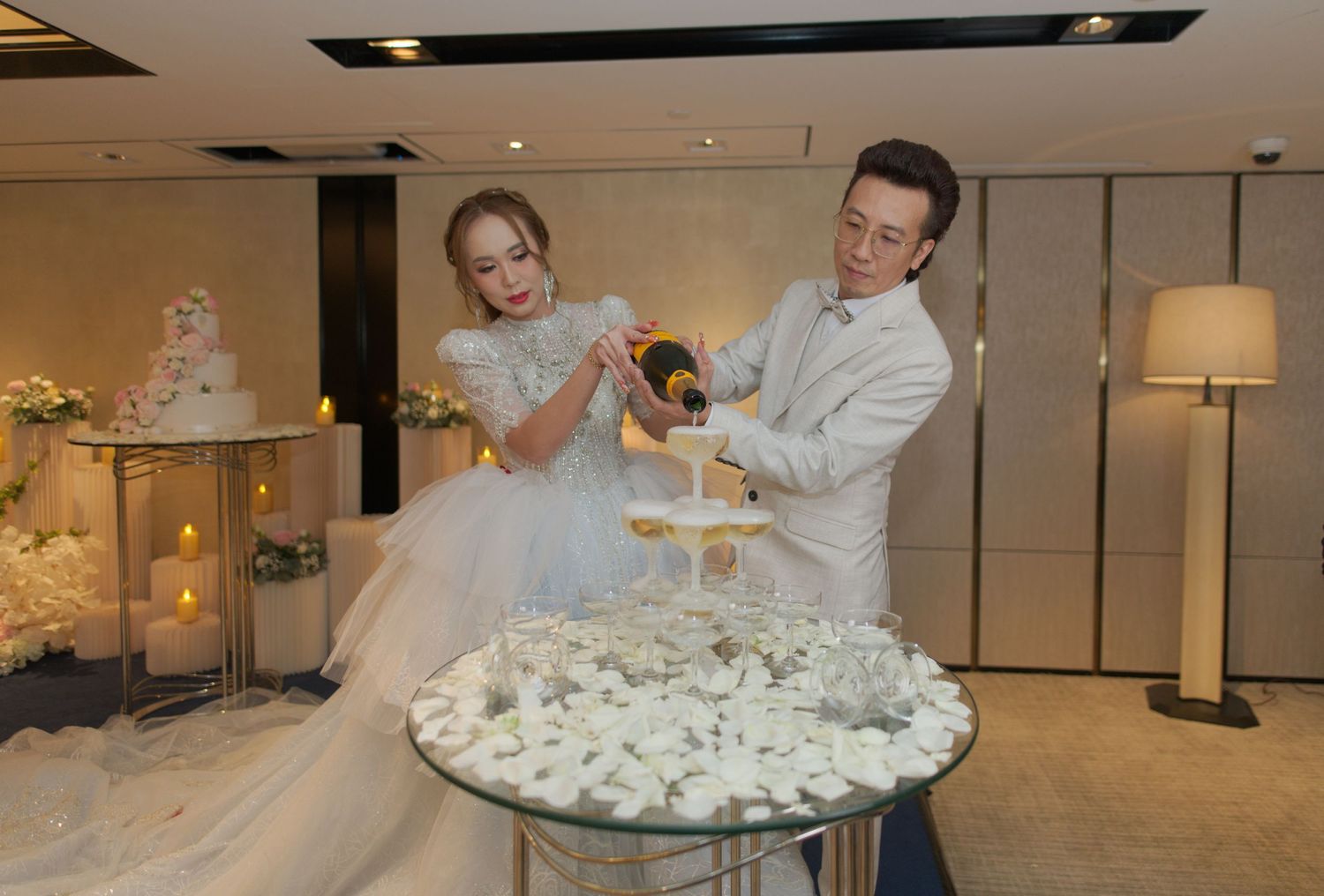 Newlyweds pouring champagne over a tower of glasses at their wedding reception.