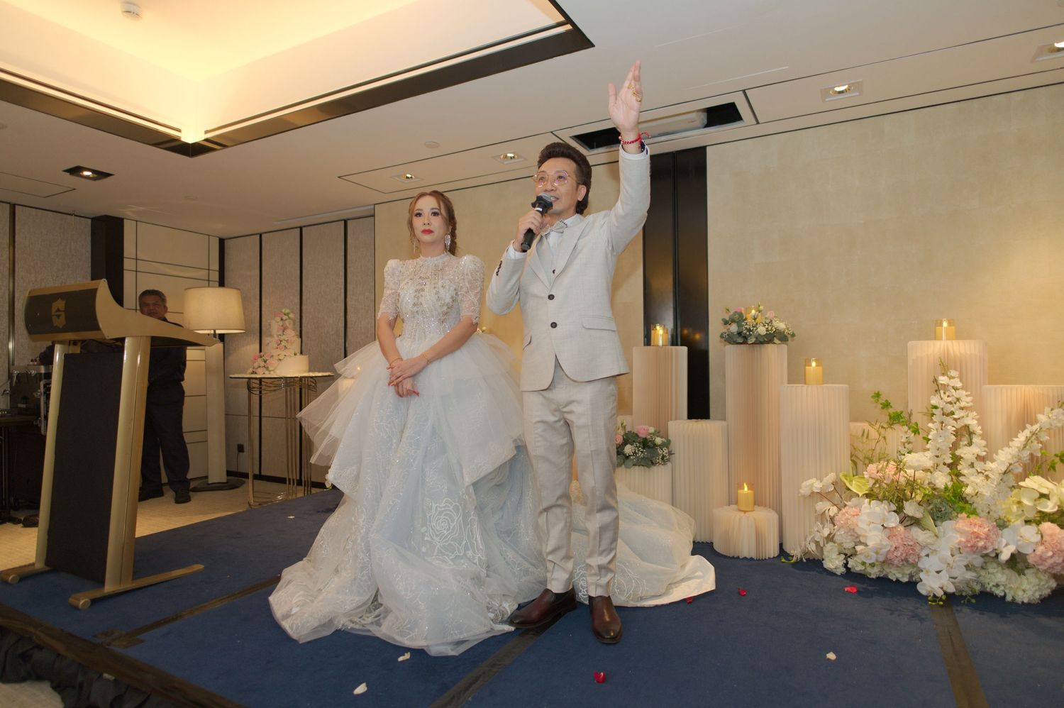 Couple performing during their wedding reception on a decorated stage with floral arrangements.