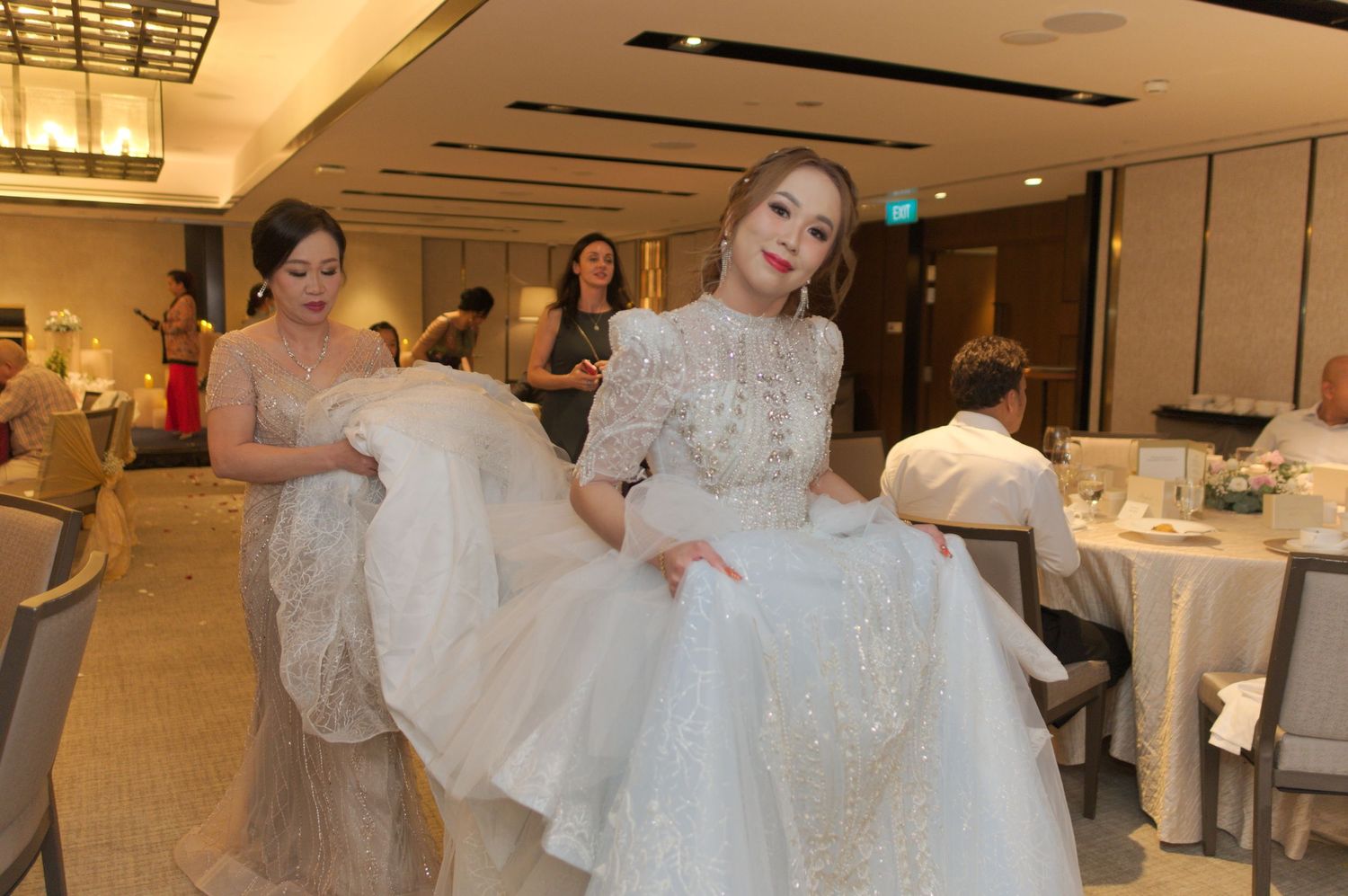Wedding dress being fluffed and arranged by attendants in an elegant reception venue.