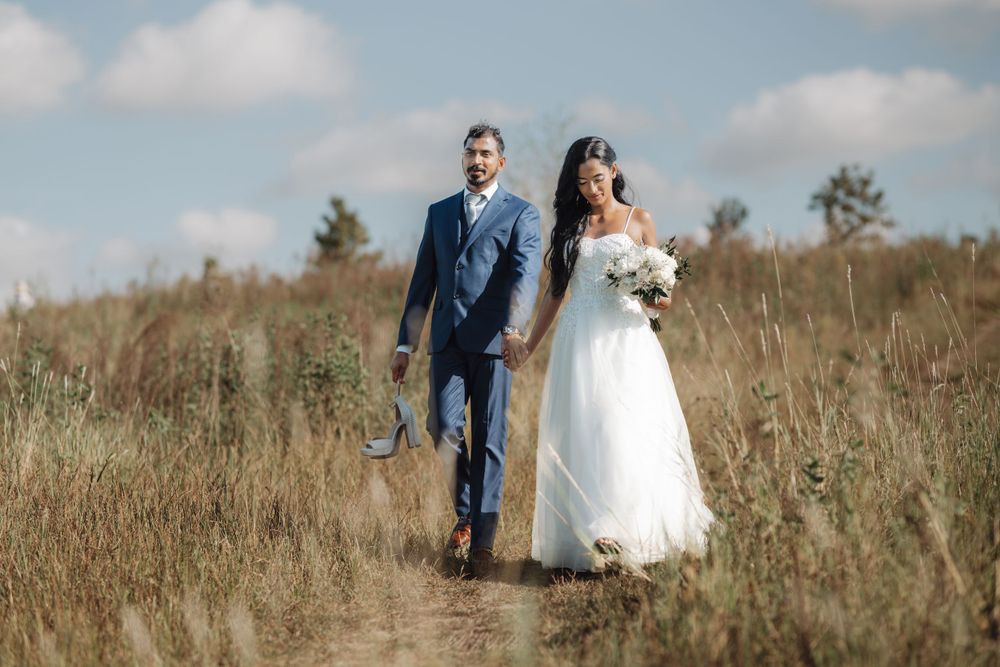 Newlyweds walking together through a rustic outdoor setting with tall grass and natural lighting.