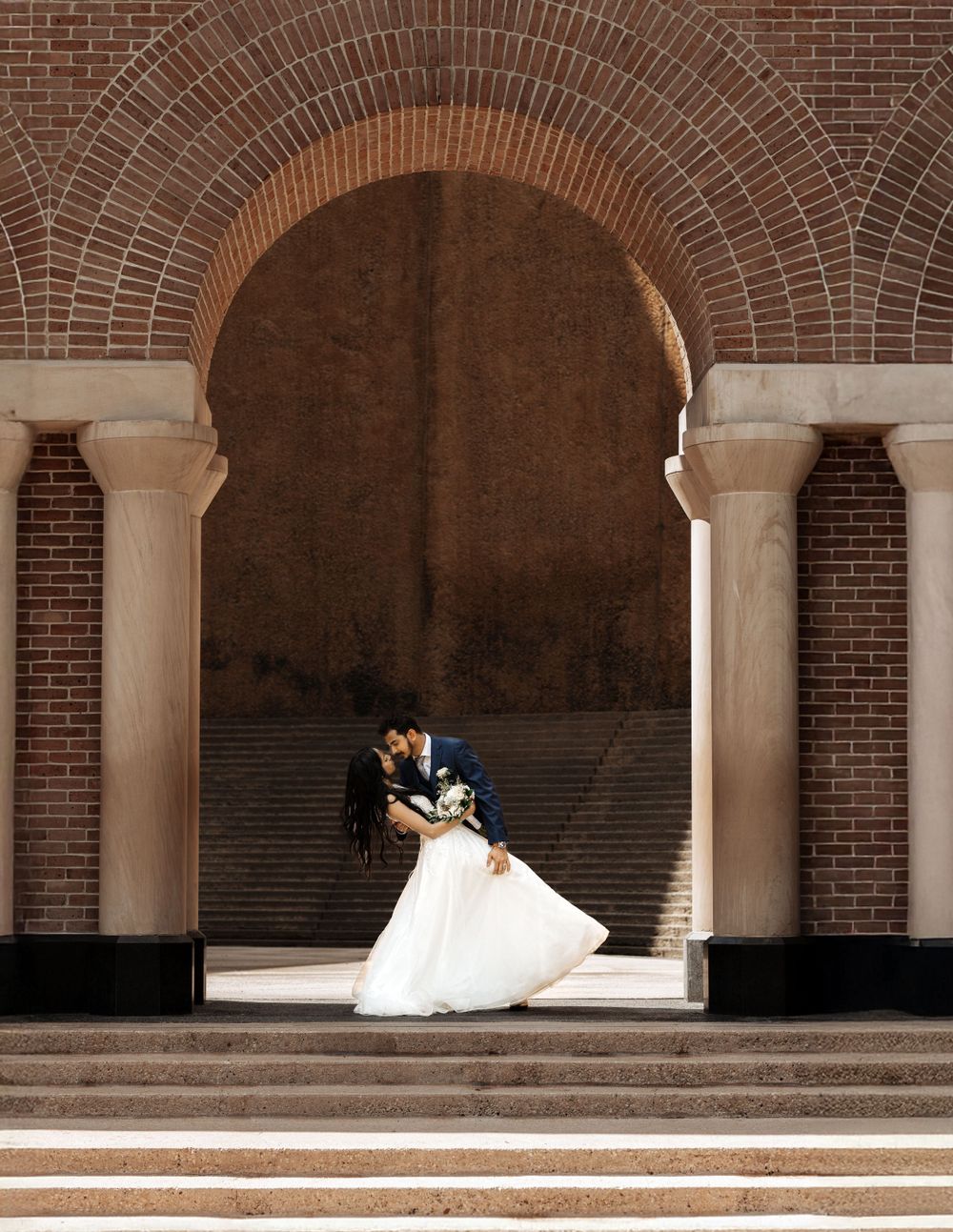 A romantic wedding moment captured under brick archways with dramatic lighting and shadows.