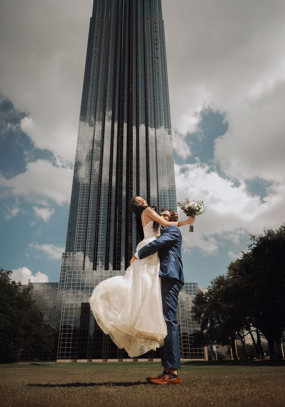 A playful wedding photo with a flowing white dress against a modern skyscraper backdrop.