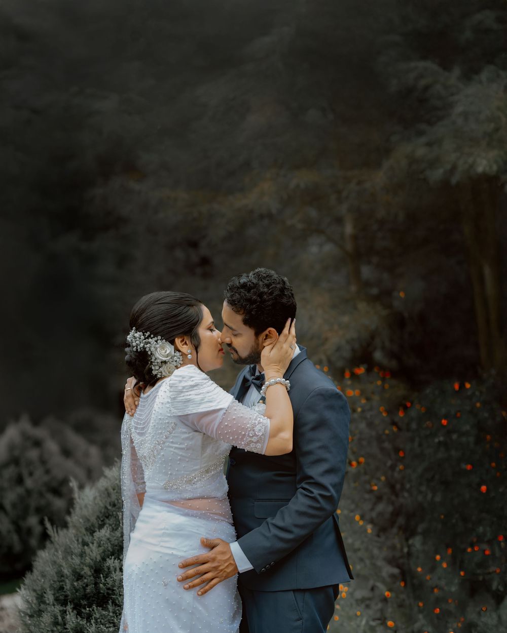 A couple shares a romantic moment in a moody outdoor setting with dark tones and glowing orange accents.