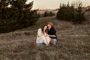Couple sitting together on a hillside at sunset surrounded by natural scenery.