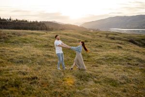Two people dance in a grassy meadow at sunset with mountains and a lake in the distance. Columbia River Gorge
