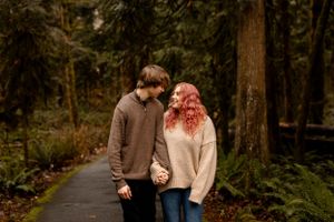 Couple walking hand in hand on a forest path surrounded by lush greenery.